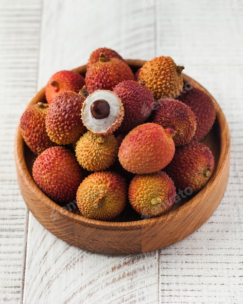 Preview: Lychees whole and half in a wooden bowl on a wooden background. Exotic fruits.