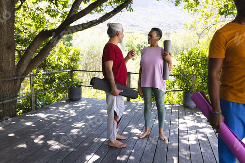 Preview: Two happy diverse senior friends talking and smiling at yoga class in sunny garden, copy space