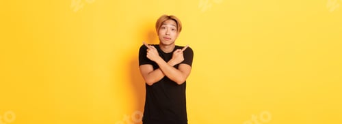 Preview: Indecisive handsome guy shrugging puzzled and pointing fingers sideways, standing yellow background