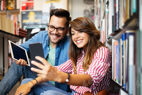 Preview: Happy beautiful hipster love student couple taking a selfie in school library