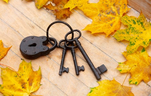 Preview: Vintage metal lock and keys with yellow maple leaves around on a table.