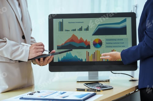 Preview: Two young Asian businesswomen sit at a table, engaged in a meeting.examine graphs and discuss