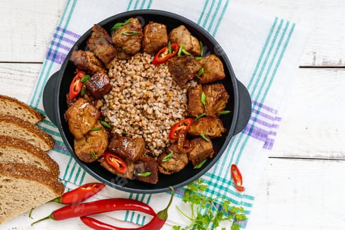 Preview: Buckwheat porridge with pieces of fried pork, served on a cast-iron frying pan.