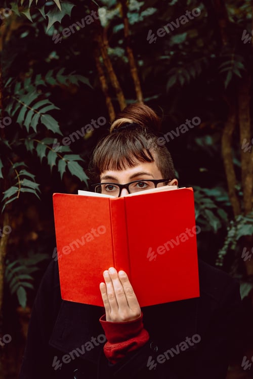 Preview: Young woman reading book on bench in park