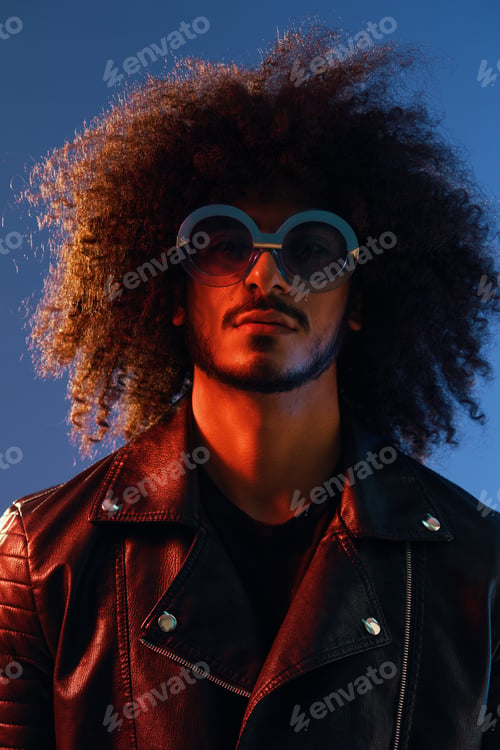 Preview: Portrait of a stylish man with curly hair with glasses smile on blue background multinational, color