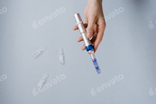 Preview: Fractional Mesotherapy Device in the Cosmetologist's Hand and Ampoules of Serum for the Skin