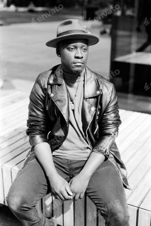 Preview: Relaxed black man sitting on bench outside in monochrome portrait.