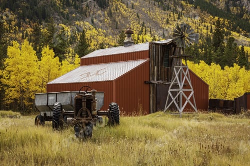 Preview: Red wooden barn and old tractor surrounded by yellow aspen trees in the countryside in Colorado