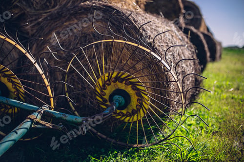 Preview: Closeup of a hay tedder with hay rolls in the background on a field