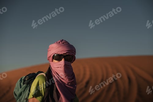Preview: Tourist wearing turban and sunglasses exploring erg chebbi dunes in merzouga desert, morocco