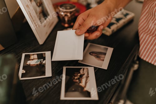 Preview: Shot of mans hand putting photo on wooden coffee table to other memorable pictures