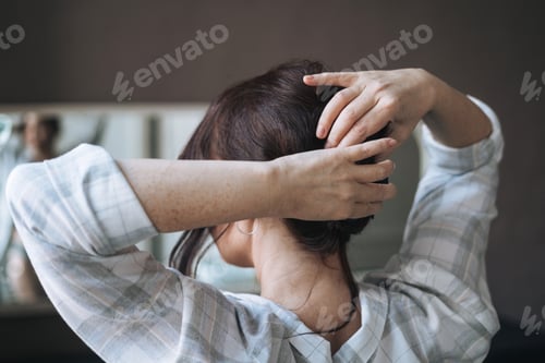 Preview: Middle aged brunette woman pins her hair in bathroom at home