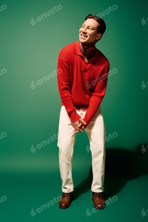 Preview: A joyful young man with tattoos dons a red sweater and white pants against a vibrant green backdrop