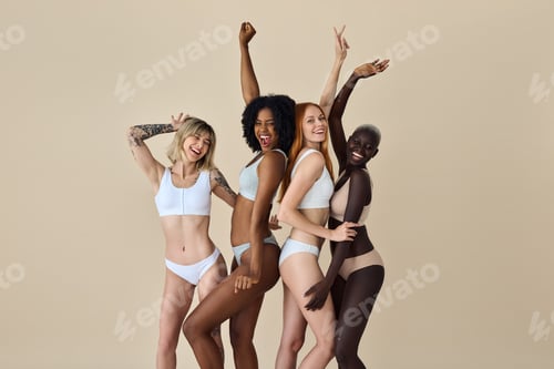 Preview: Happy diverse young women wearing underwear dancing on beige background.