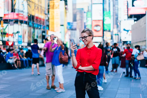 Preview: Caucasian female standing in crowded square with mobile phone in hands