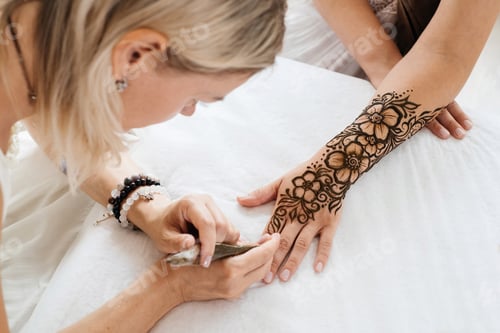 Preview: female hands with mehendi pattern of flowers, artist painting with henna