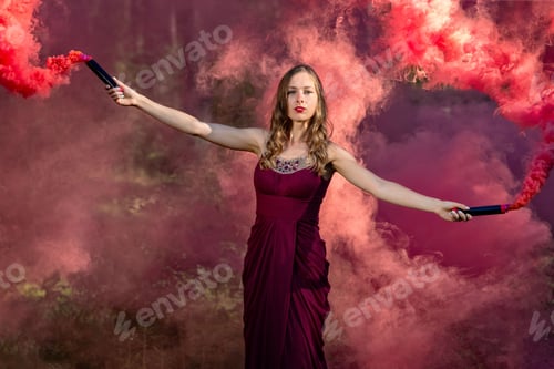 Preview: Young beautiful woman in red evening dress and red smoke candles in hands.
