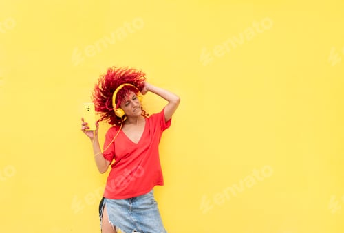 Preview: a latin woman with red afro hair listening to music on her headphones dancing on a yellow background