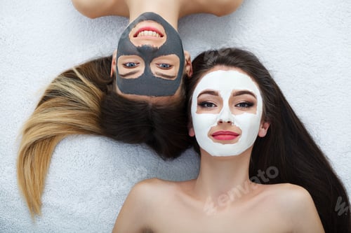 Preview: Home spa. Two women holding pieces of cucumber on their faces lying the bed.
