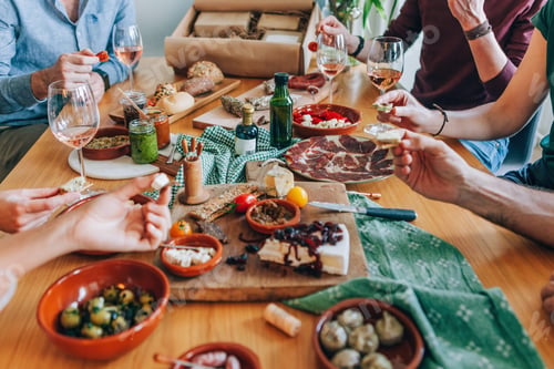 Preview: unrecognizable people sitting around a table - friends have an aperitif from food box delivered