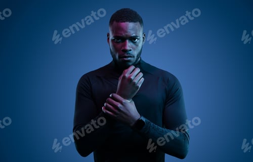 Preview: Brutal young black male athlete touching wrist in blue studio