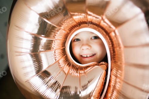 Preview: Young pretty birthday girl's face through the circle round hole in the balloon with number nine
