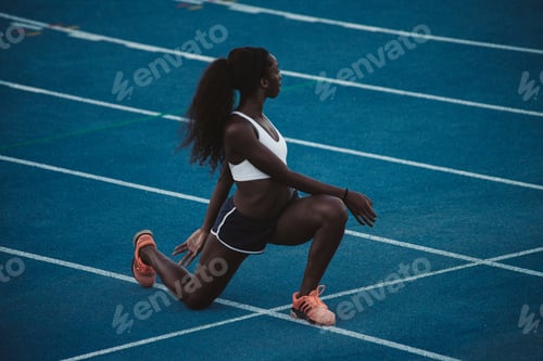 Preview: A black athlete of African origin performs stretching exercises on a blue athletics track.