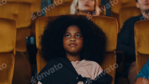 Preview: Attractive cheerful young black african girl laughing while watching film in movie theater.