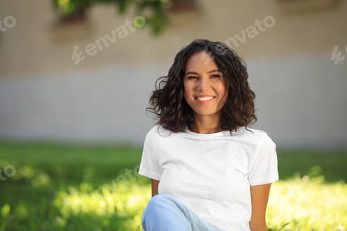 Preview: Happy young woman sitting on green grass in park on sunny day