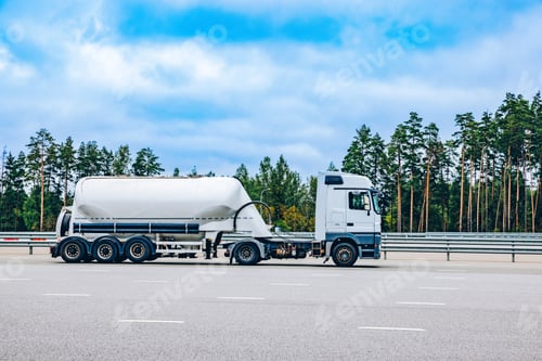 Preview: A White Cement Truck on the Highway Traveling Through Lush Green Forests Under a Clear Blue Sky