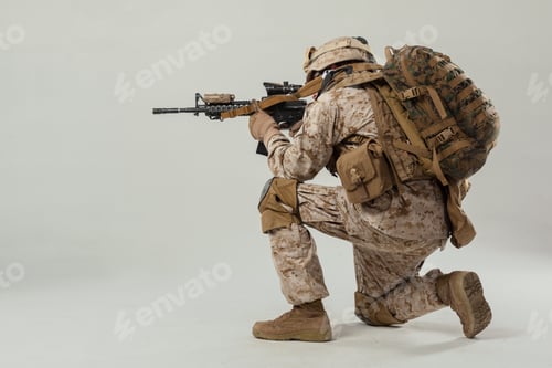 Preview: Soldier in combat gear holds rifle while kneeling on neutral background in training session