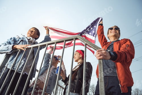 Preview: teenagers having fun and waving american flag in skateboard park, hipster style concept