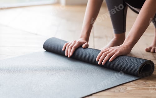 Preview: Woman Rolling Out Yoga Mat on Wooden Floor