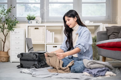 Preview: Asian woman thinking and folding cloth while packing or organizing luggage in bedroom or living room