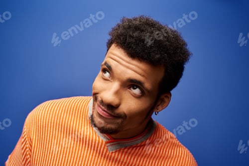 Preview: Handsome man with curly hair gazing upwards in vibrant orange and blue setting