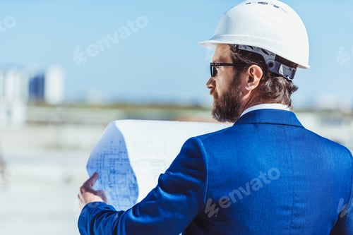 Preview: Businessman in hardhat and suit examining building plans