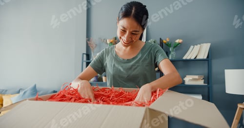 Preview: Happy beautiful Asia lady unboxing cardboard delivery package from online marketplace.