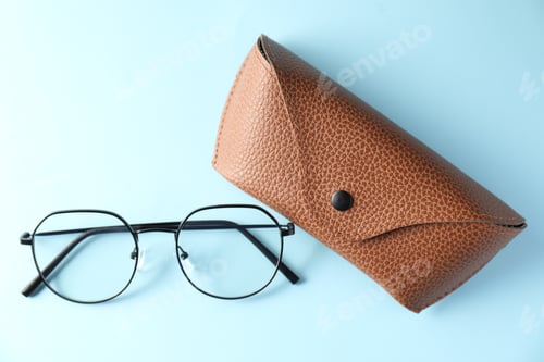 Preview: Case with stylish glasses on light blue background, flat lay