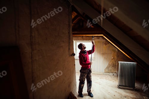 Preview: Full length of man with work tool renovating attic