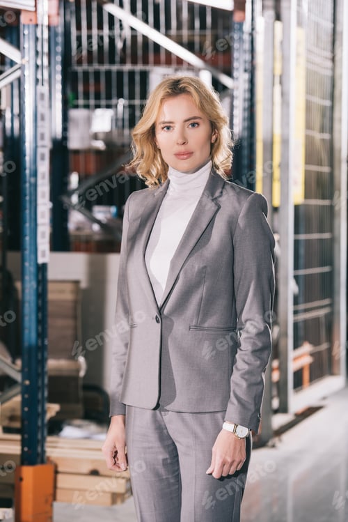 Preview: confident businesswoman in formal wear looking at camera while standing in warehouse