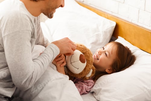 Preview: Little girl lying in bed in morning, hugging teddy bear
