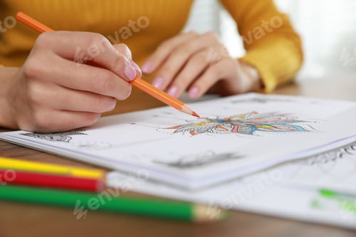 Preview: Young woman coloring antistress page at table indoors, closeup