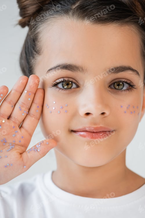 Preview: portrait of adorable girl with lip gloss and sparkling glitter stars on face looking at camera