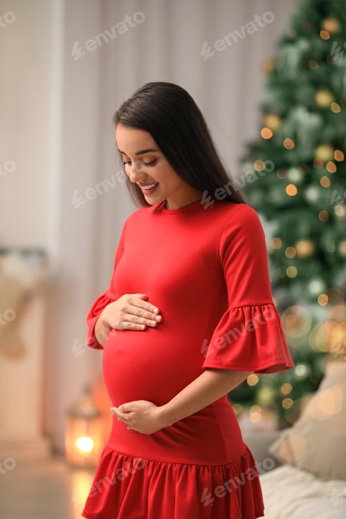 Preview: Happy pregnant woman in room decorated for Christmas. Expecting baby