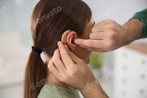 Preview: Young man putting hearing aid in woman's ear indoors