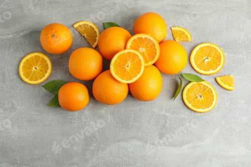 Preview: Many ripe oranges and leaves with space for text on grey table, top view