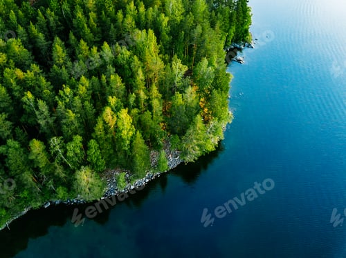 Preview: Aerial view of blue lake with stone coast and green tree forests on a sunny summer day in Finland.