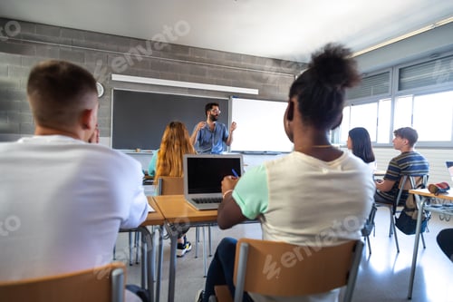 Preview: Rear view of teen high school students in classroom listen to male teacher explaining lesson.