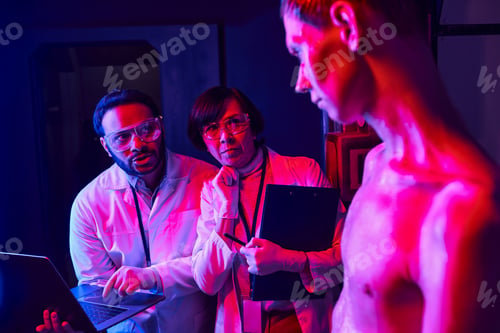 Preview: extraterrestrial humanoid looking at multiethnic scientists with laptop in innovation laboratory