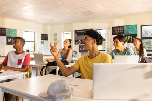 Preview: In high school, teenagers using laptops and raising hands in classroom discussion